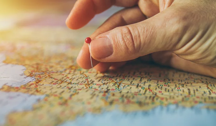 A hand holding a pin, hovering above a map (Image by piviso from Pixabey).