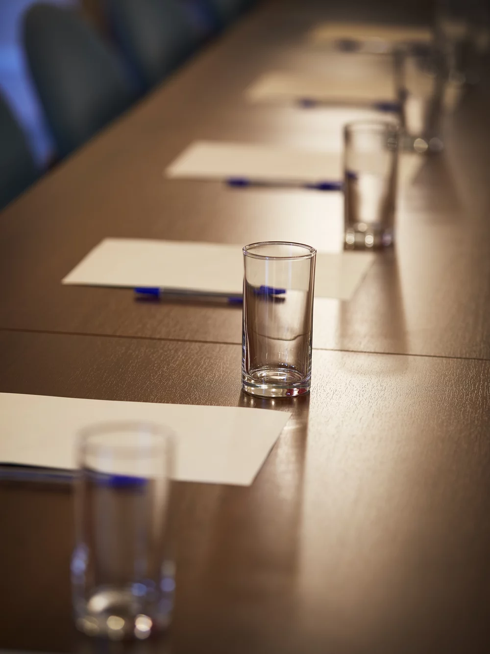 A table in the GHIL Conference Room, with paper pads, pens, and water glasses laid out ready for a conference. Light shines down from above and illuminated the objects.