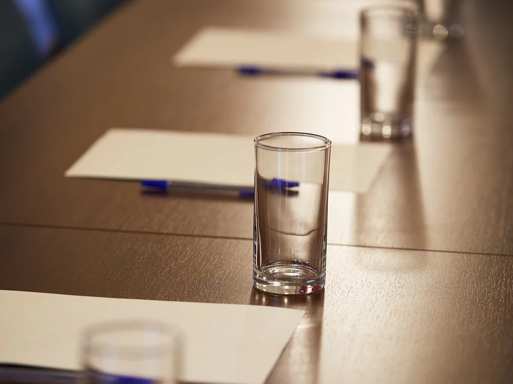 A table in the GHIL Conference Room, with paper pads, pens, and water glasses laid out ready for a conference. Light shines down from above and illuminated the objects.