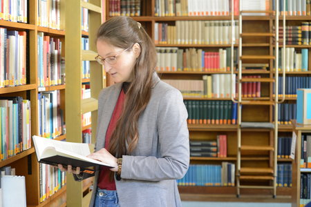 An intern looking up information in a book, with the wooden library bookcases behind her
