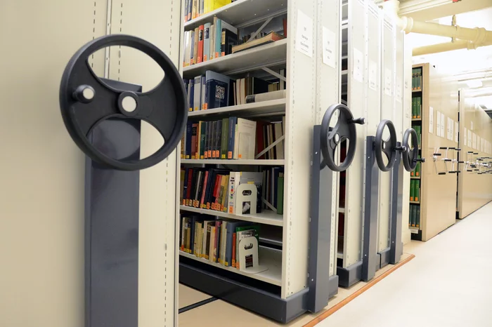 Movable library shelving units with books, the wheels to move the roller racking can be seen in the foreground.