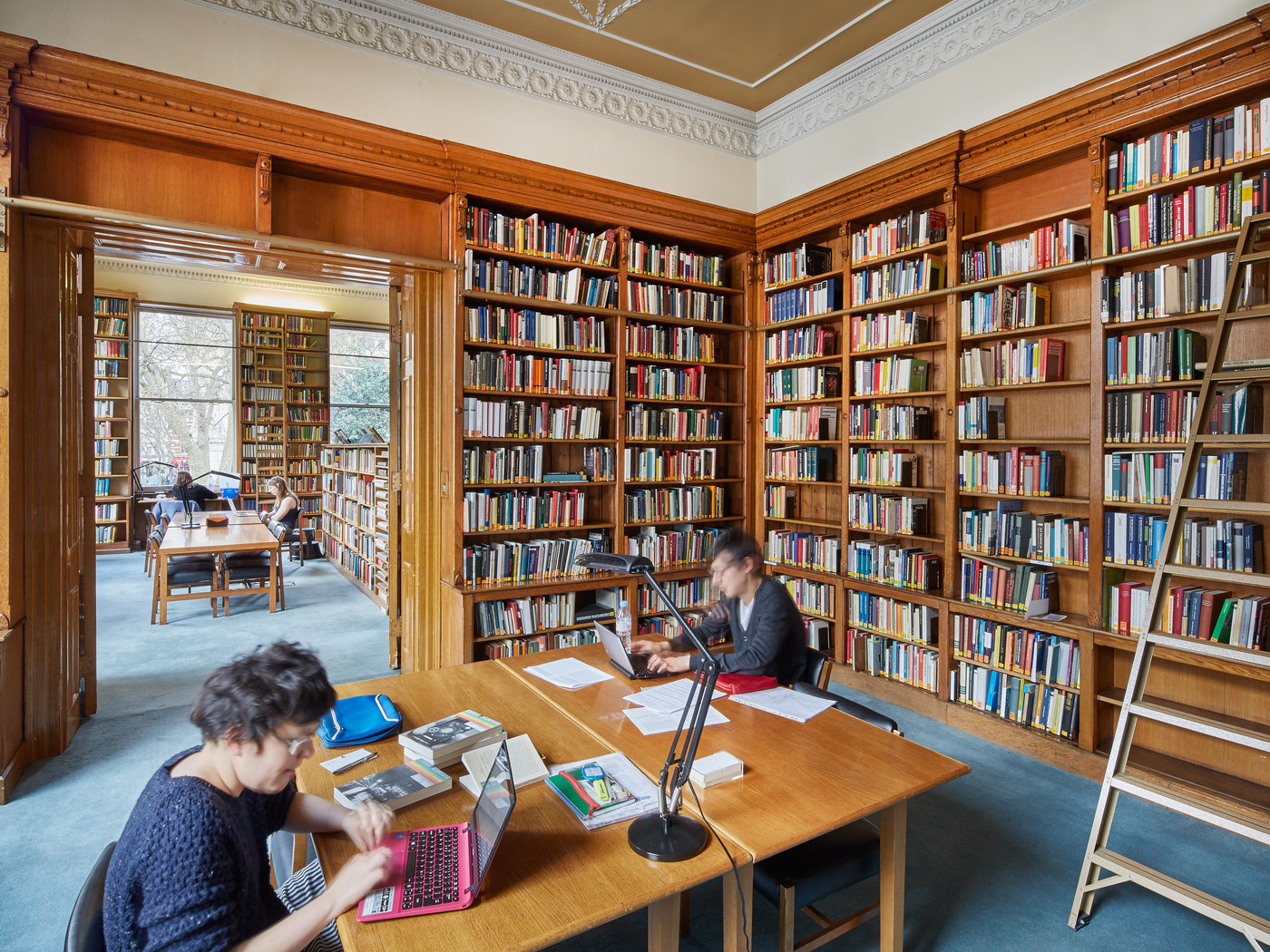 Two readers studying in one of the first floor reading rooms, with bookshelves and a ladder in the background