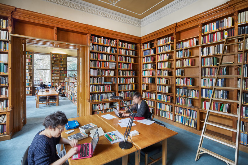 Two readers studying in one of the first floor reading rooms, with bookshelves and a ladder in the background