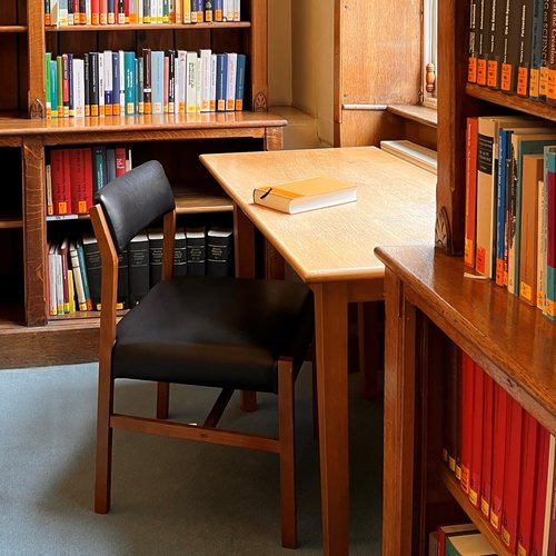 Image showing a desk and chair in one of the first floor library rooms. The chair is pulled out invitingly, and a book is lying on the desk.