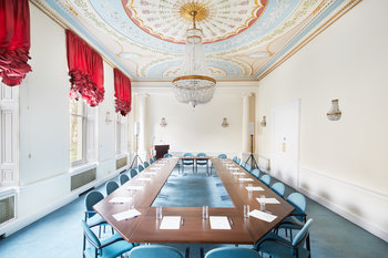 Image of the main conference room, set up for a conference, with paper, pens and drinking glasses set out at each place on the tables.