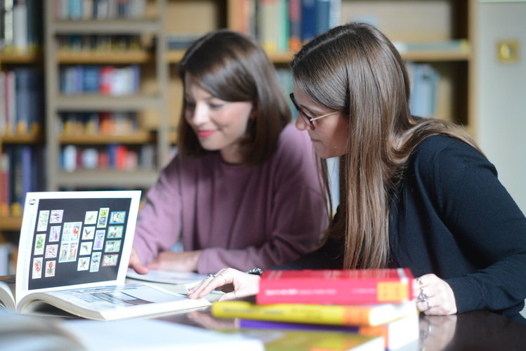 Two students looking at several books spread out over one of the library desks.