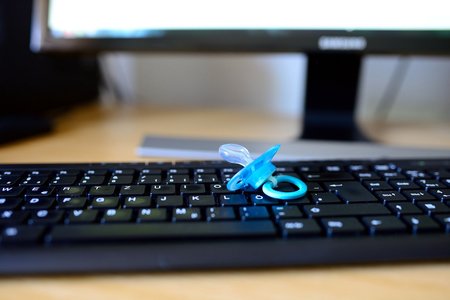 A blue infant dummy/pacifier/soother on a computer keyboard on an office desk