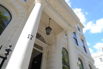 The front entrance of the GHIL, taken from the left at a low angle, showcasing the portico and pillars and showing a portion of blue sky in the upper right-hand corner.