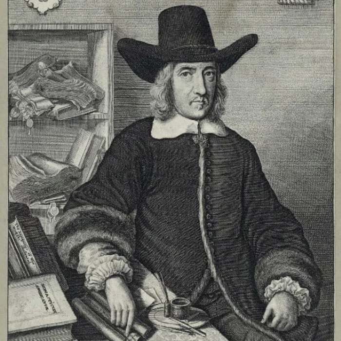 Etching of Sir William Dugdale, by Wenceslaus Hollar, 1656. The image shows Dugdale seated, with a desk covered with books and scrolls to his right. His hand rests lightly on a scroll, which sits next to an inkwell. He is wearing a coat with large fur cuffs. His white shirt collar and the ruffs at the ends of his sleeves are visible. He has on his head a large hat. Behind him on his right side are shelves with more scrolls.