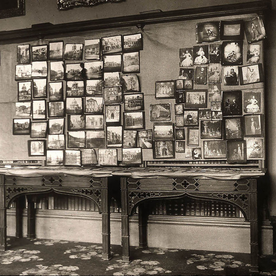 Image of a room of the centenary photography exhibition, held at Lacock Abbey, 1934, which depicts several tables and wall covered with a selection of Fox Talbot's photographs