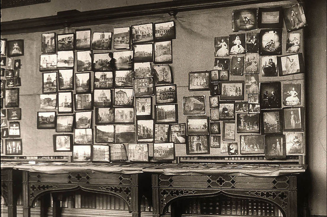 Image of a room of the centenary photography exhibition, held at Lacock Abbey, 1934, which depicts several tables and wall covered with a selection of Fox Talbot's photographs