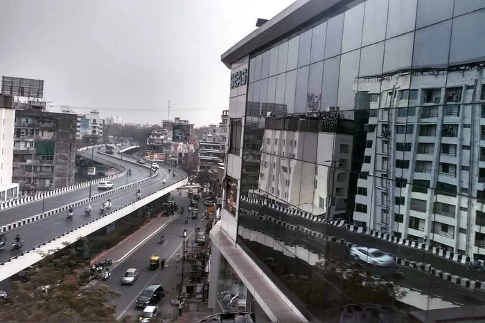 A major thoroughfare in Mumbai, with roads on two levels, the building on the other side of the road are reflected from the glass facade of a modern building.