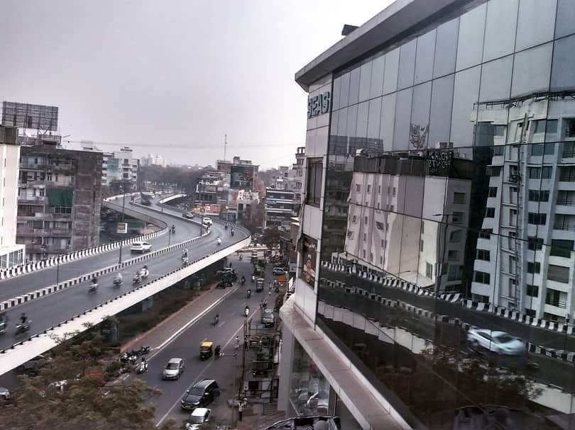 A major thoroughfare in Mumbai, with roads on two levels, the building on the other side of the road are reflected from the glass facade of a modern building
