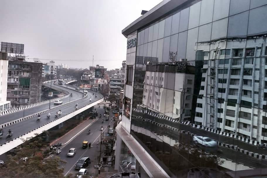 A major thoroughfare in Mumbai, with roads on two levels, the building on the other side of the road are reflected from the glass facade of a modern building