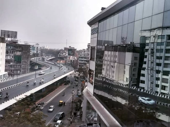 A major thoroughfare in Mumbai, with roads on two levels, the building on the other side of the road are reflected from the glass facade of a modern building.