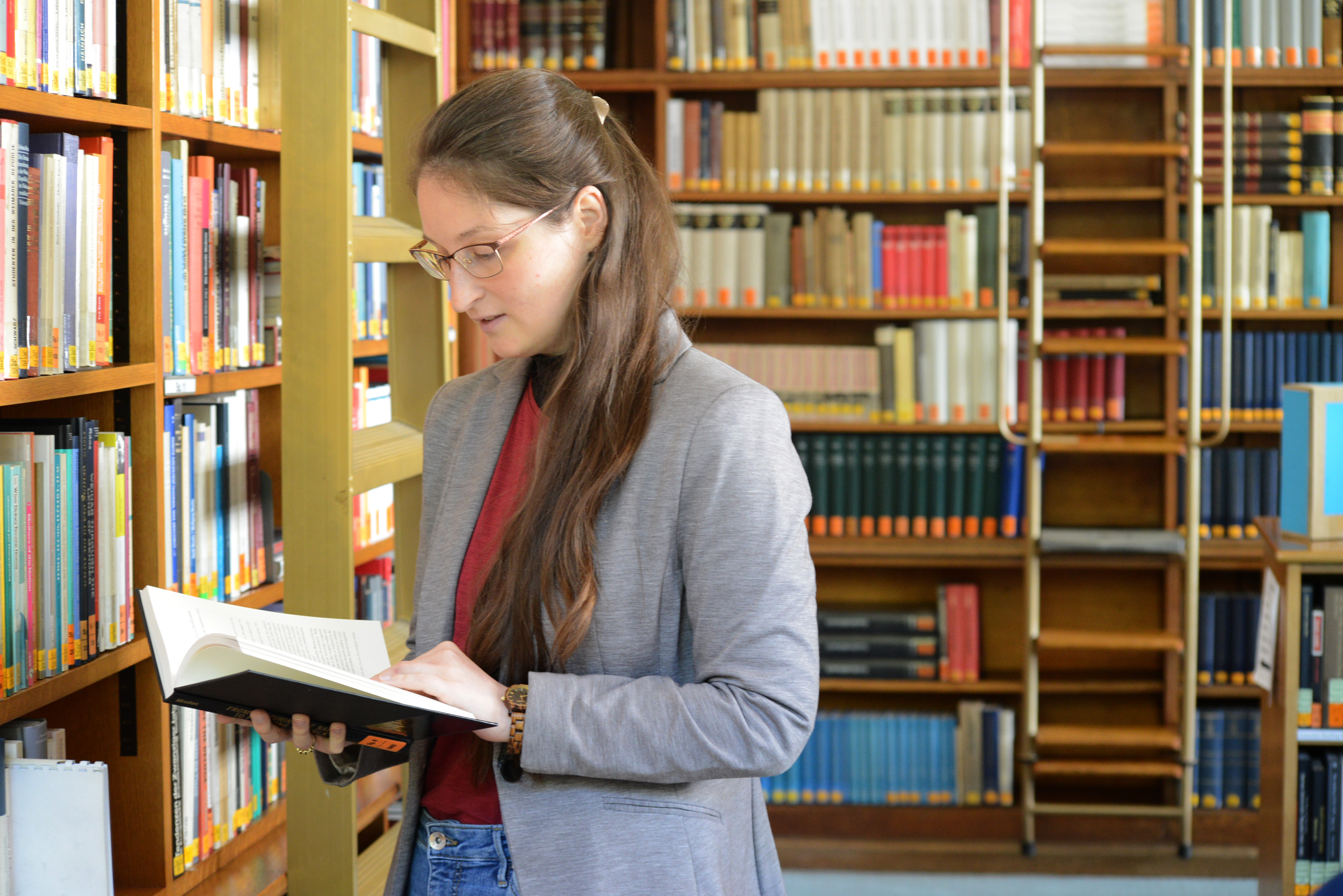 An intern looking up information in a book, with the wooden library bookcases behind her